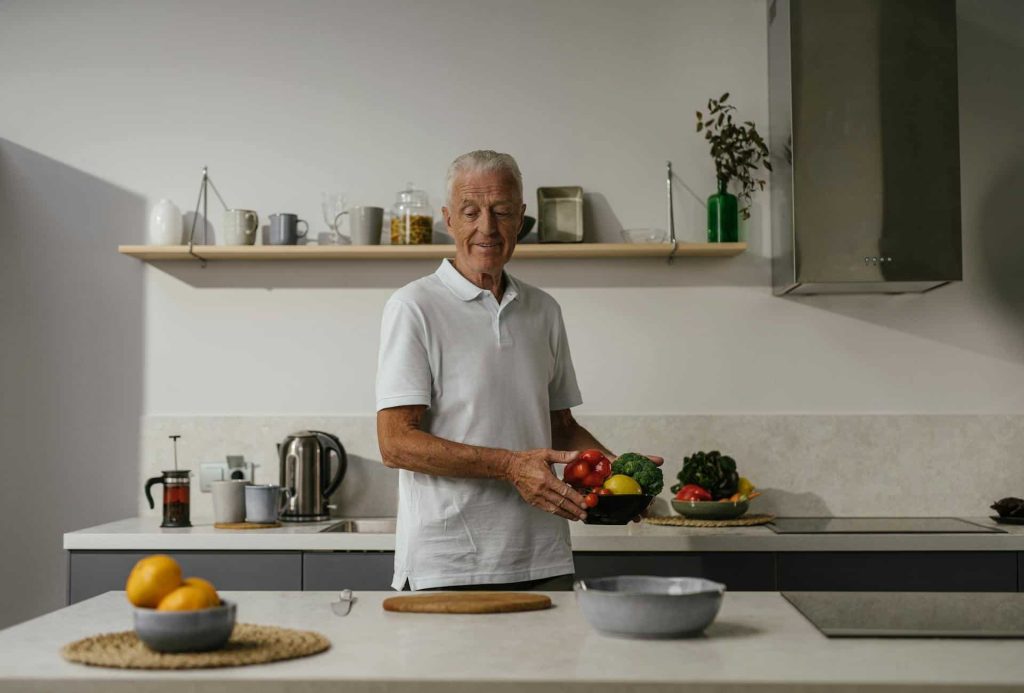 elderly man in white polo shirt holding a bowl of vegetables