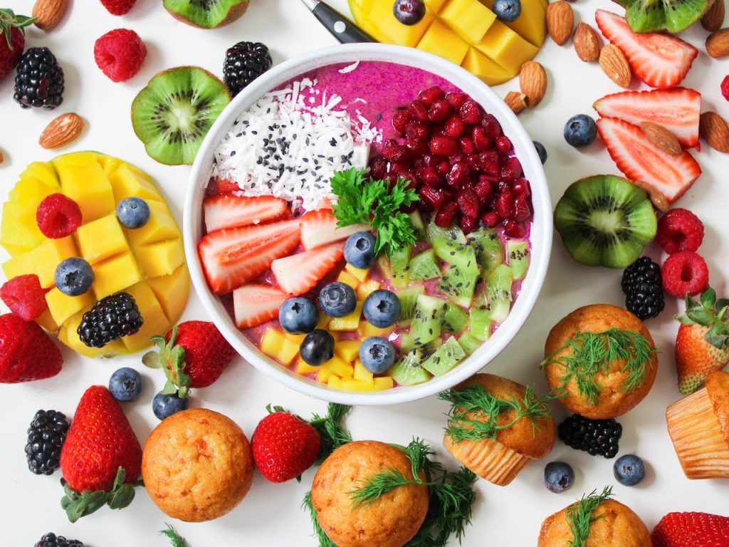 a bowl of freshly cut fruits surrounded by muffins and sliced fruits