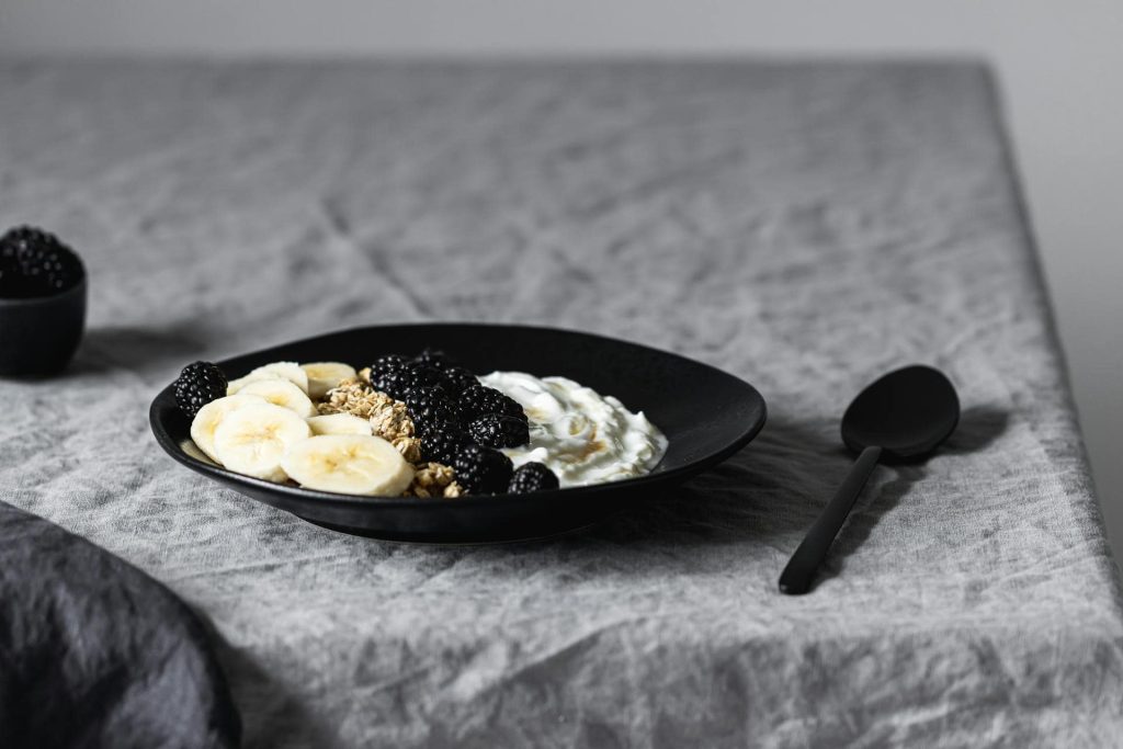 banana slices, berries and yogurt in black plate