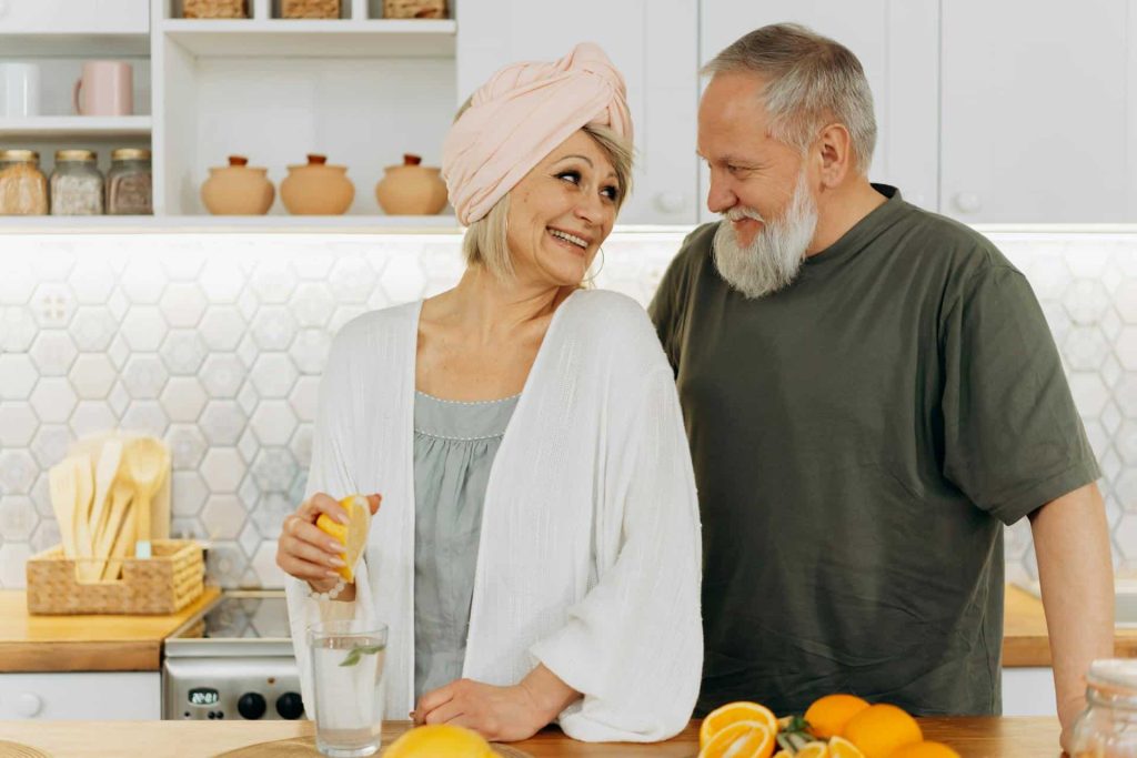 elderly woman squeezing lemons while looking at her husband
Image Source