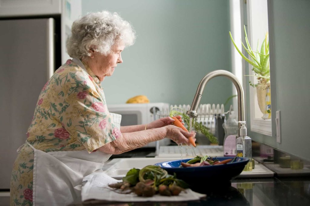 elderly woman wearing yellow and pink floral dress washing vegetables